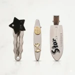 A set of assorted hair clips, containing 3 metal clips in different designs and sizes: one with a gold heart, another with a black logo, and a third with a black and white smiley face design. High-quality handmade craftsmanship, perfect for everyday use - Wateen store