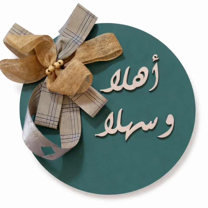 علاقة باب خشبية مصنوعة يدويًا من خشب عالي الكثافة (HDF)، دائرة نصف قطرها 30 سم، مزينة بعبارة "أهلًا وسهلًا" وتفاصيل أنيقة على شكل فيونكة